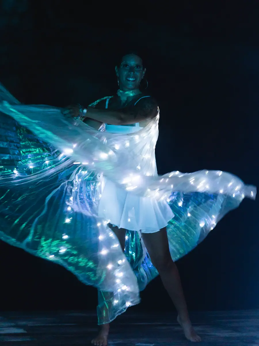 Dancer spinning with blue and green LED wing lights on a dark stage