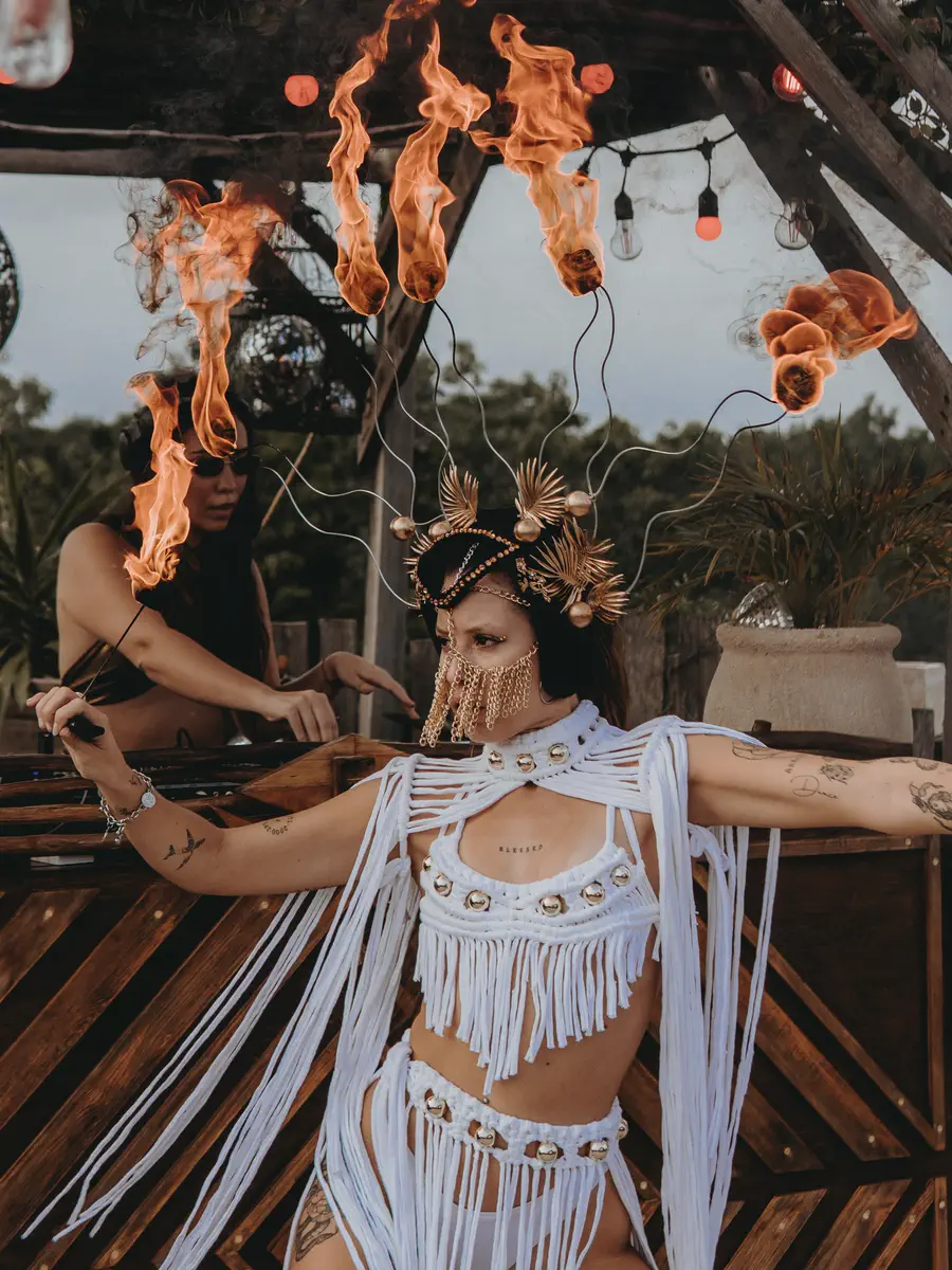 Two performers in white fringe costumes with lit headpieces at an outdoor venue