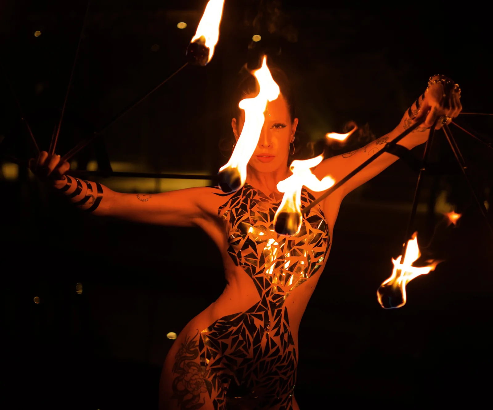 Karu, founder of Escena Global, with painted body opening two lit fire fans at night