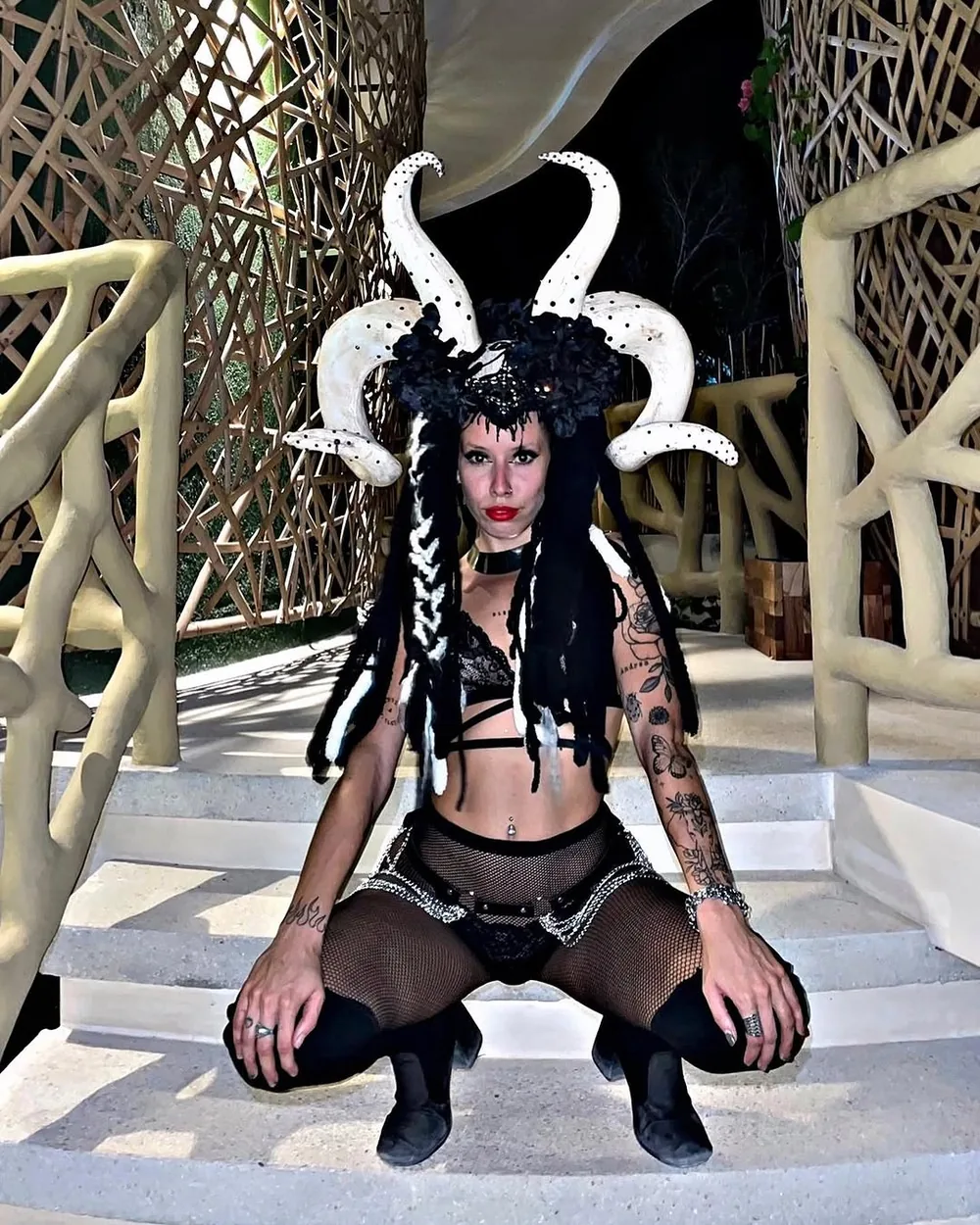 Performer with a horned headpiece and black costume, crouched on a white staircase